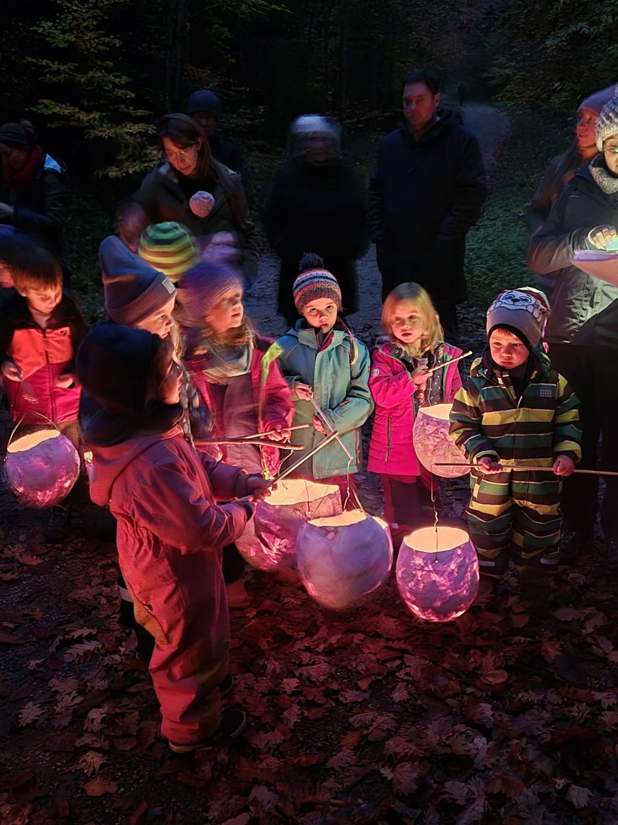 Herbst bei den Waldstrolchen: Kinder mit selbst gebastelten, leuchtenden Laternen beim Laternenlauf im dunklen Wald