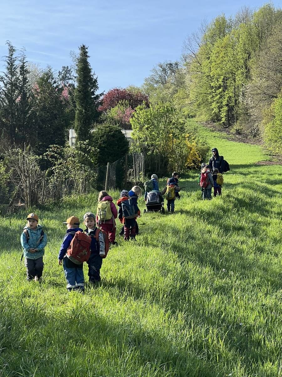 Waldstrolche unterwegs: Kinder mit Rucksäcken laufen über die Frühlingswiese zum Wald