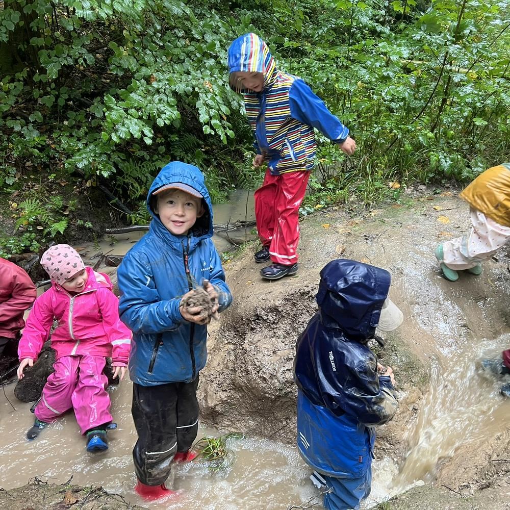 Kinder in Matschhosen und Gummistiefeln spielen im Bachlauf