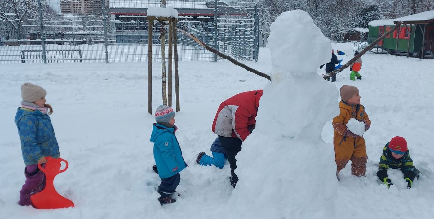 Winter bei den Waldstrolchen: Kinder bauen gemeinsam einen großen Schneemann mit Ast-Armen